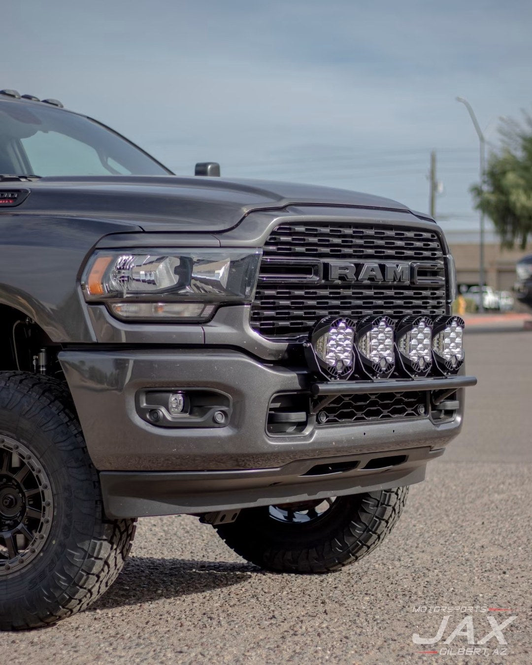 Front-end detail of the Ram 2500 showing custom bull bar with four Baja Designs LP9 lights, RAM grille, and Innov8 G600 wheel with Toyo AT3 tire