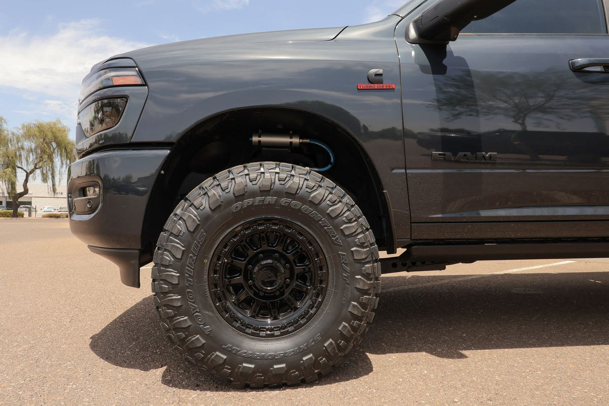 Close-up of a 17x9 gloss black Arena Enduro wheel with a 37x12.50R17 Toyo Open Country R/T Pro tire and Carli shock reservoir in the wheel well