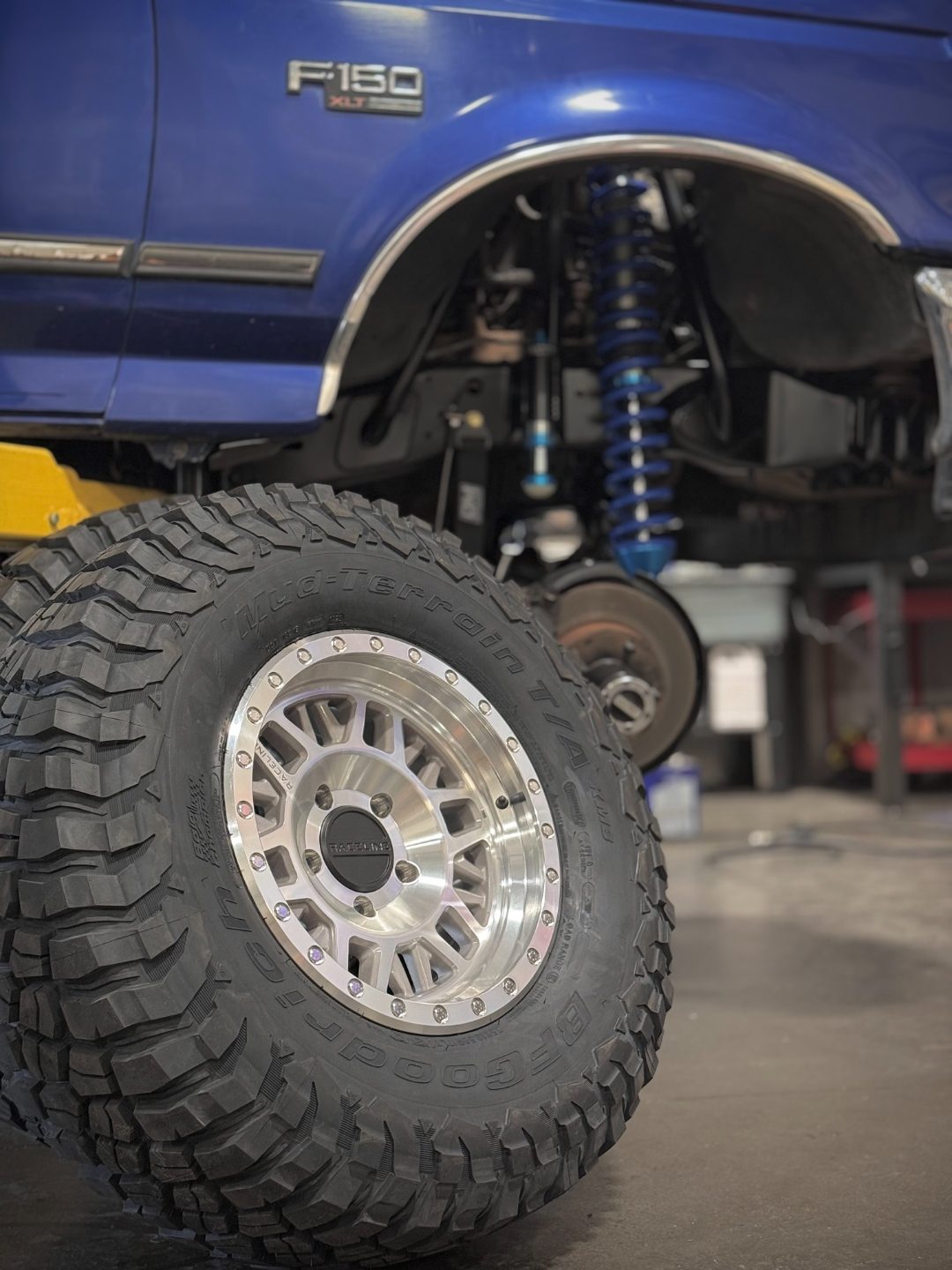 Close-up of the polished Raceline beadlock wheel and BFGoodrich KM3 tire with blue King coilovers behind