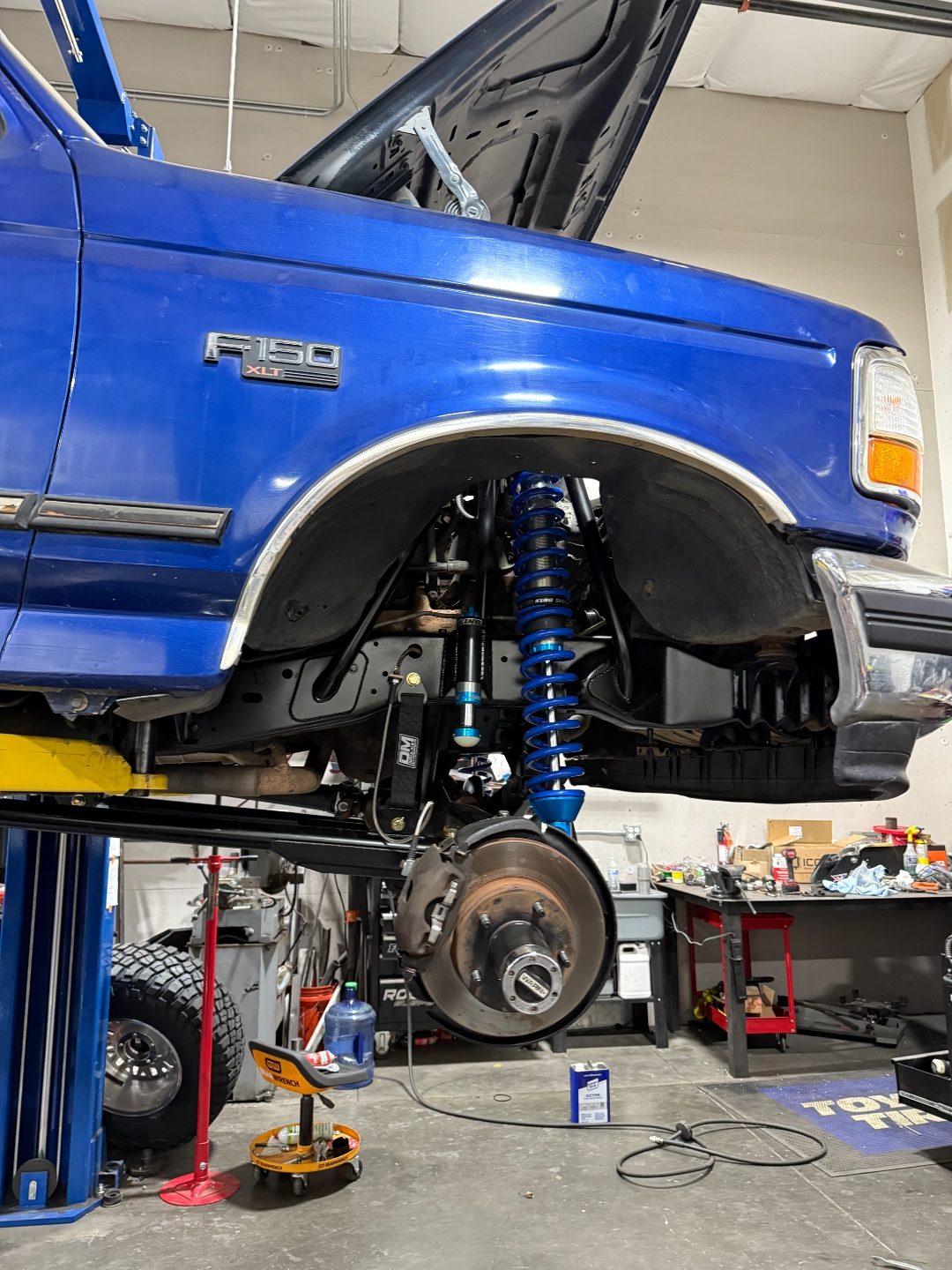 Front suspension with the wheel off — blue King coilover, black King bypass shock, Desolate limit strap, and Warn locking hub
